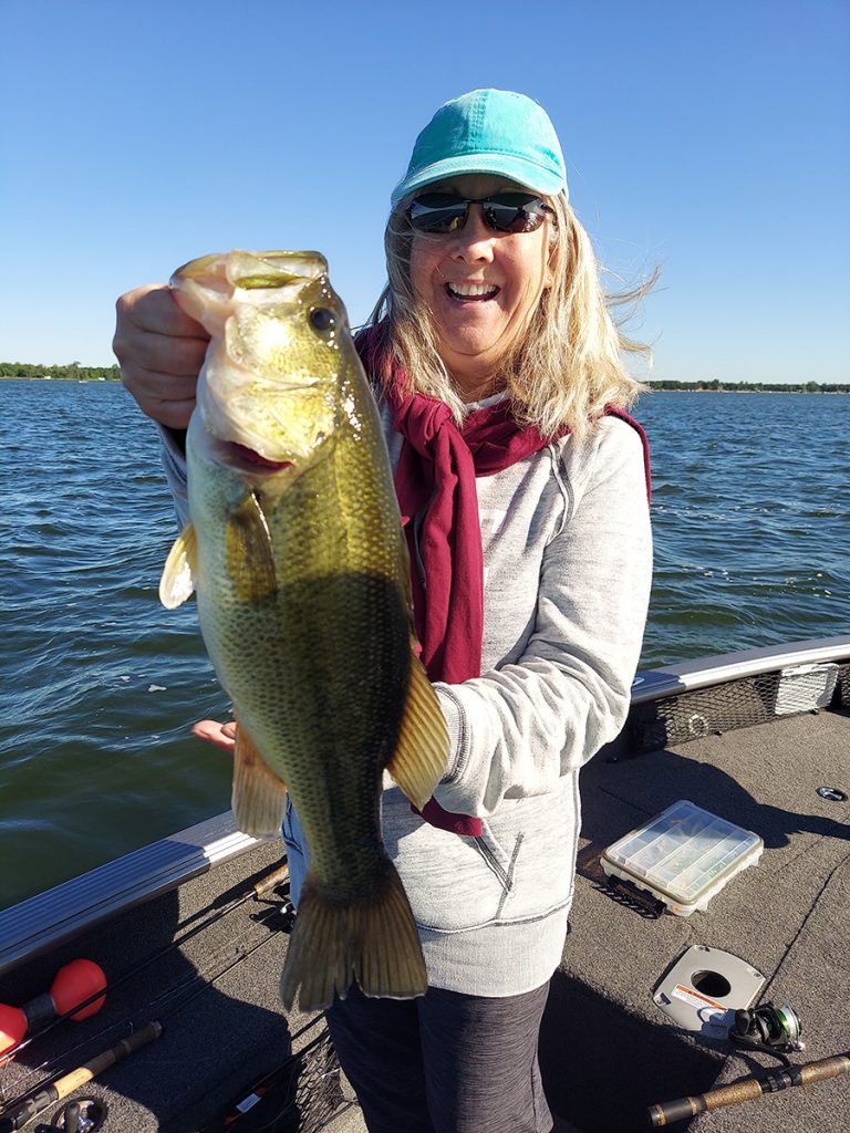 a woman shows off the large mouth bass she caught on a boat in Fridley Minnesota
