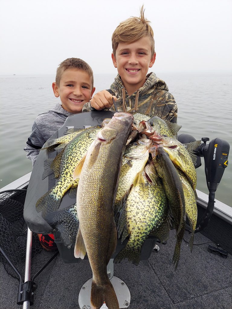 two boys pose with lots of croppies and walleye they caught fishing on a lake