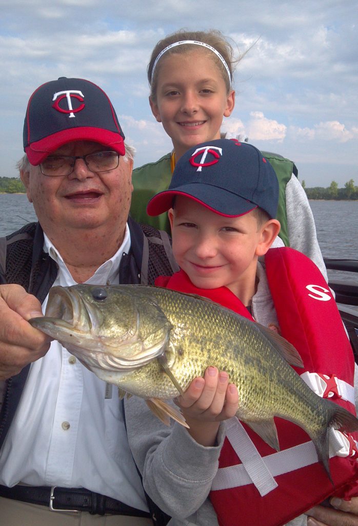 grandpa and grandkids pose with a huge large mouth bass they caught on a lake