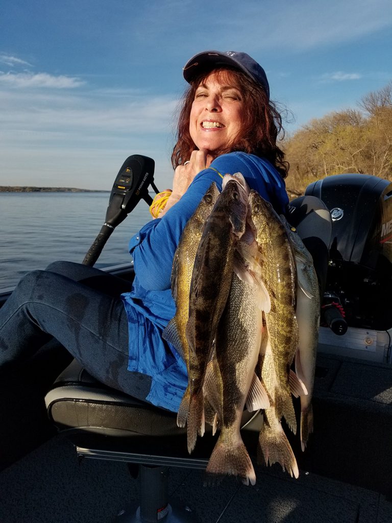 woman poses in boat with walleyes she caught on a lake in Minnesota