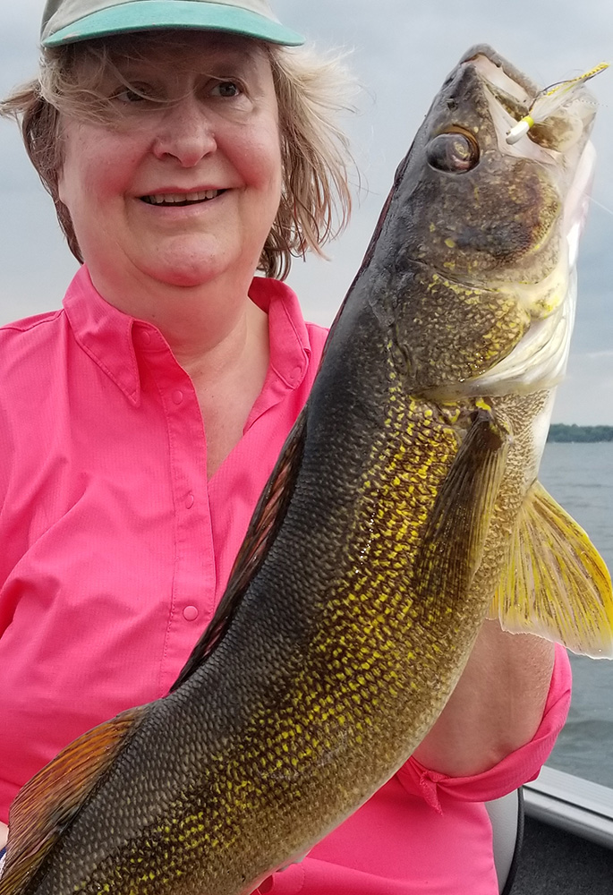 a woman in a pink shirt shows off the huge walleye she caught on a lake in northwestern Minnesota