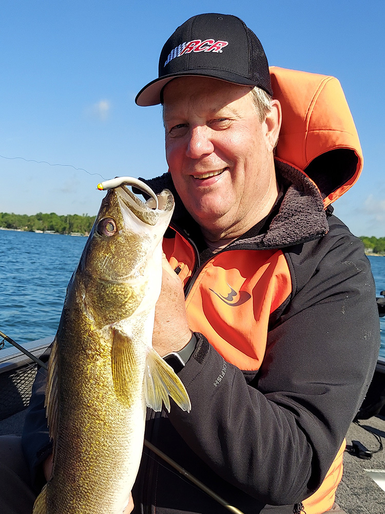 a man smiles with the walleye he caught while fishing from a boat on a Minnesota lake