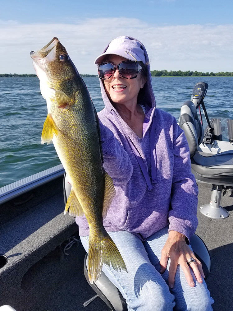 a woman holds up the large walleye she caught with fishing guide Steve Carney on a lake in Minnesota